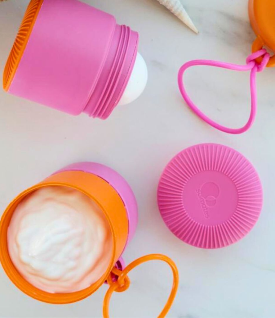 Three pink and orange silicone containers sit on a light-colored surface. Two are open—one with a white cream-like substance inside, the other revealing a white ball-shaped item. Perfect for female entrepreneurs starting a business, these containers have loop handles for easy carrying.