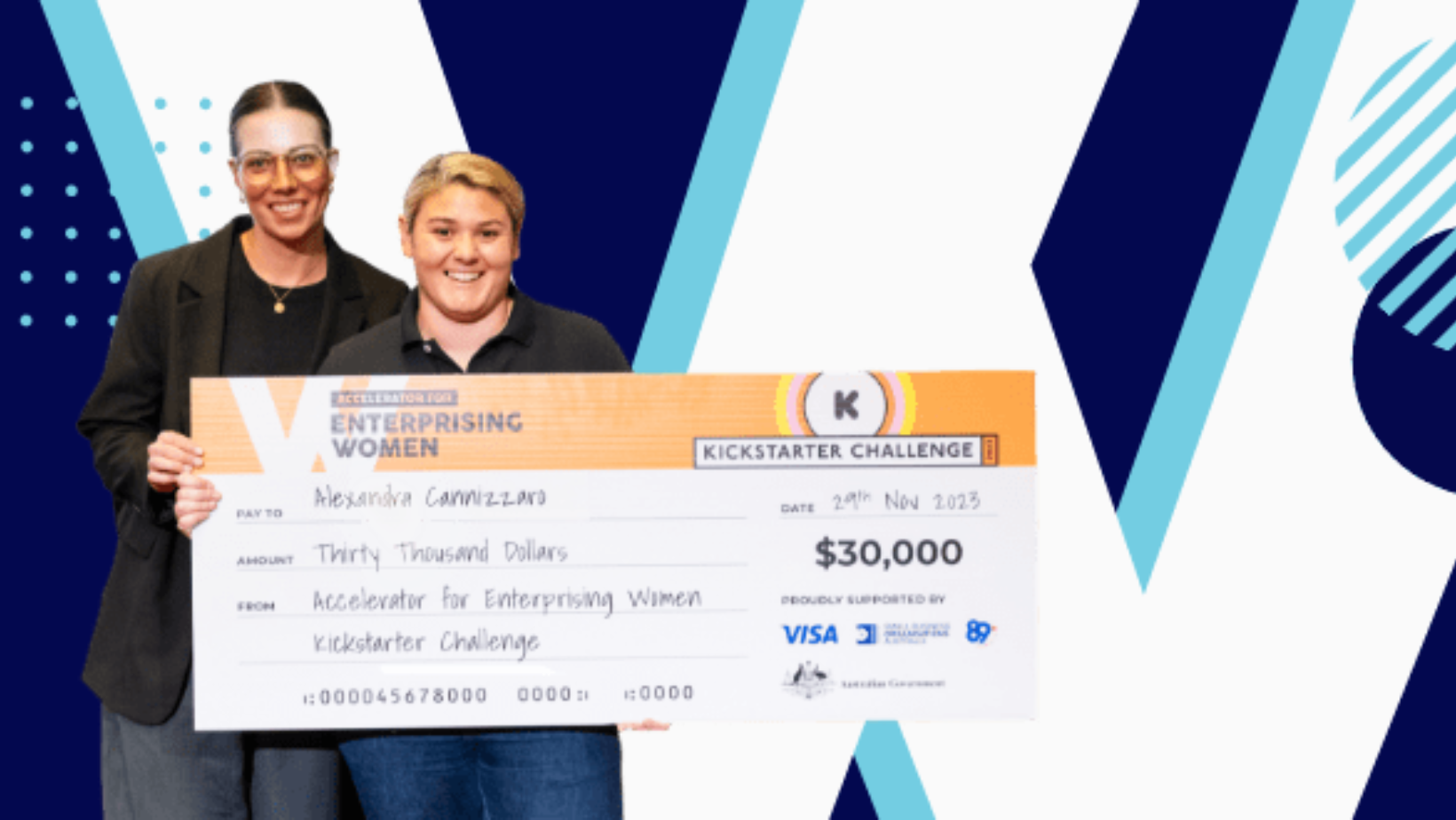 Two individuals smile while holding a large presentation check. The check reads "Enterprising Women Kickstarter Challenge," is dated November 29th, 2023, for the amount of $30,000, and is made out to Alessandra Cavacece. Celebrating women in business, the background features a blue and white pattern.