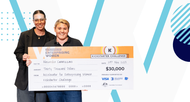 Two people are holding a large check together. The check is made out to Alessandra Cannizzaro from the Accelerator for Enterprising Women Kickstarter Challenge, dated November 29, 2023, for $30,000. The background features a modern, geometric design celebrating innovative business ideas for women.