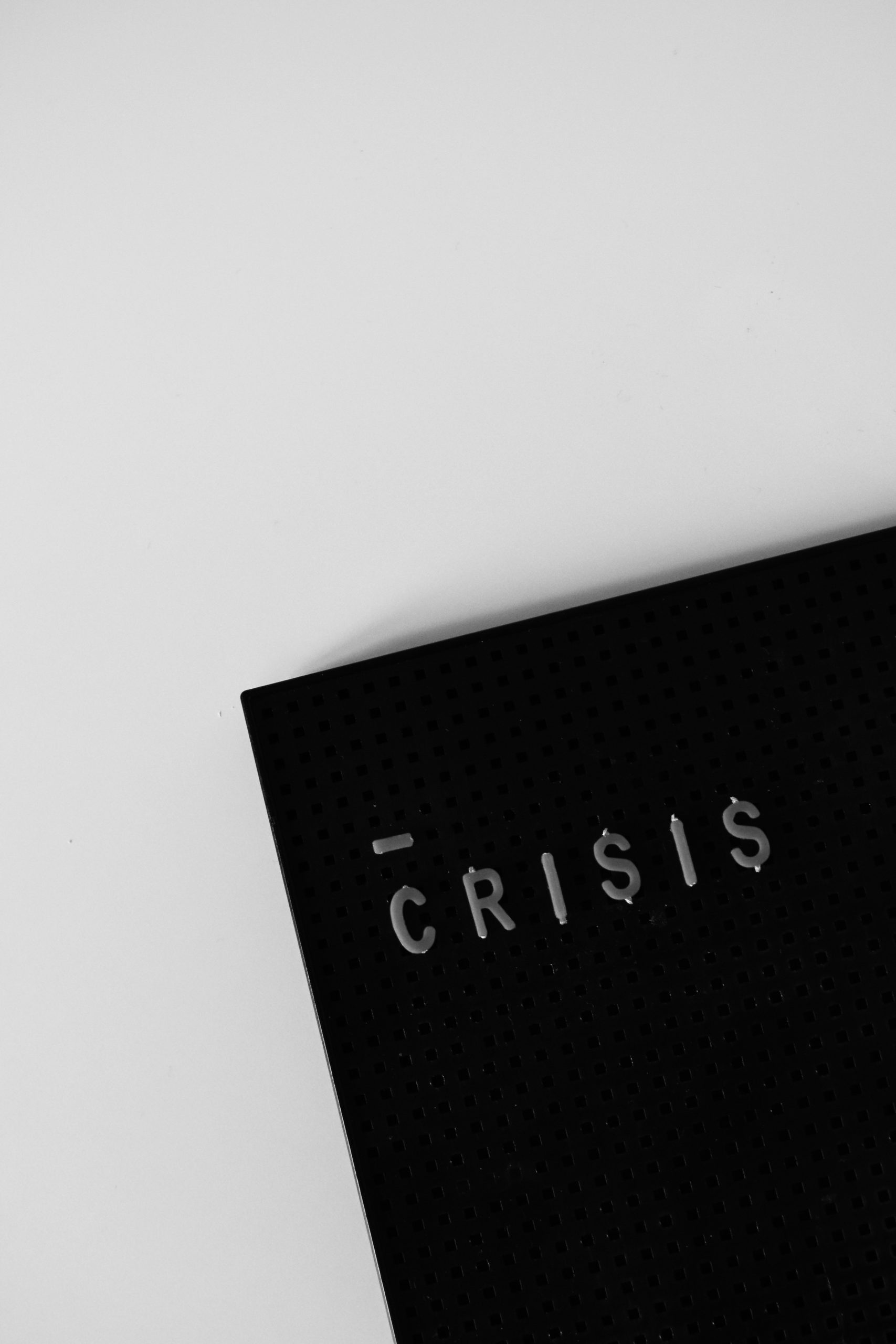 A black pegboard with the word "CRI$I$" written on it in white letters, creatively symbolizing entrepreneurial challenges. The pegboard is placed on a white background, offering a poignant message for aspiring female businesses.