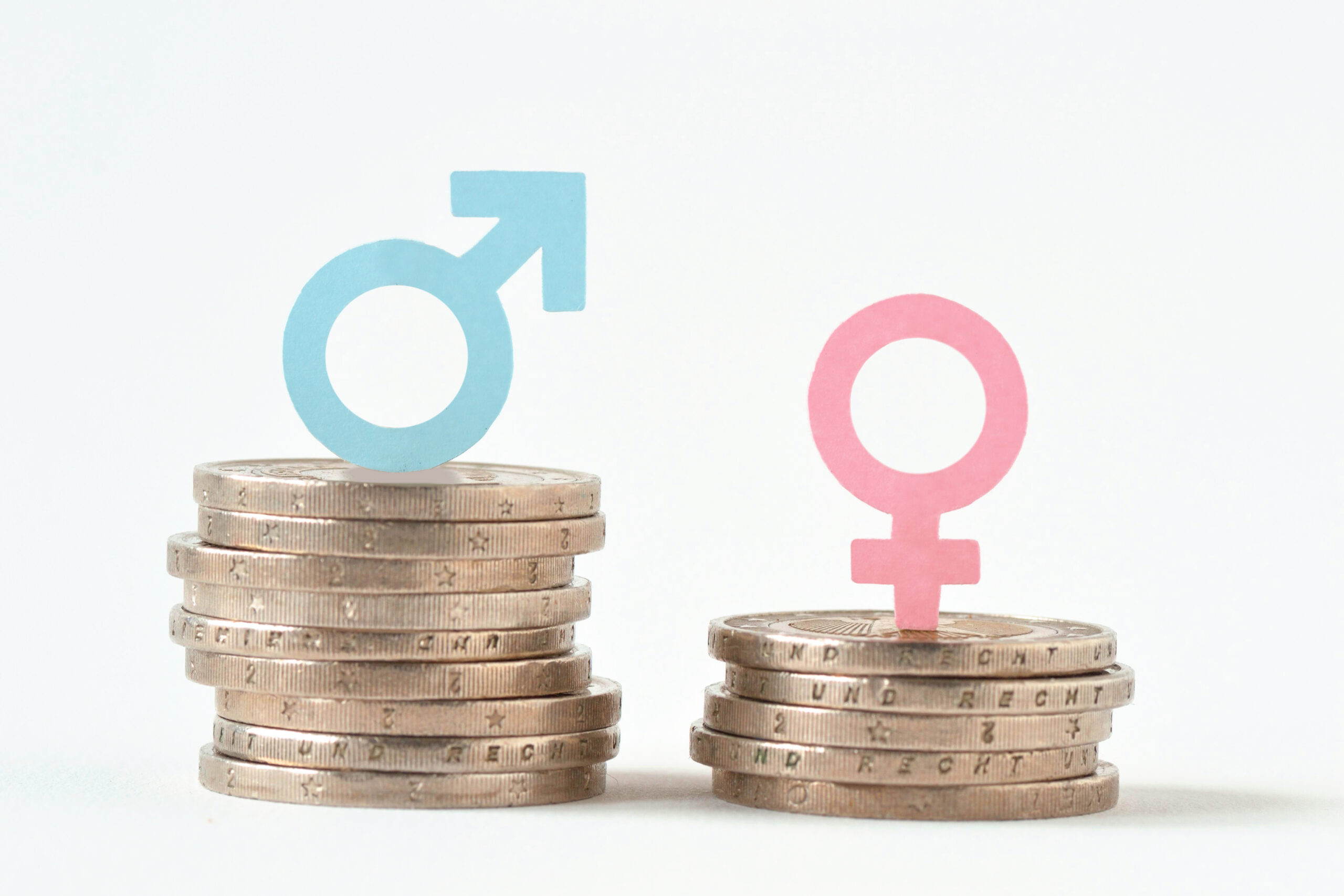A stack of 10 coins with a blue male gender symbol on top is next to a smaller stack of 5 coins with a pink female gender symbol on top, highlighting the gender pay gap. This disparity underscores the importance of supporting women in business and encouraging innovative business ideas for women.